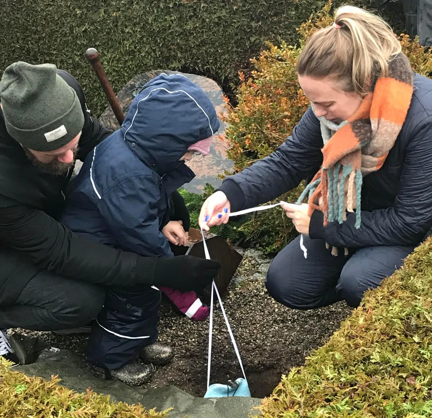 Parret og deres fireårige datter sænker her en urne af uld ned i jorden. Foto: Privat.