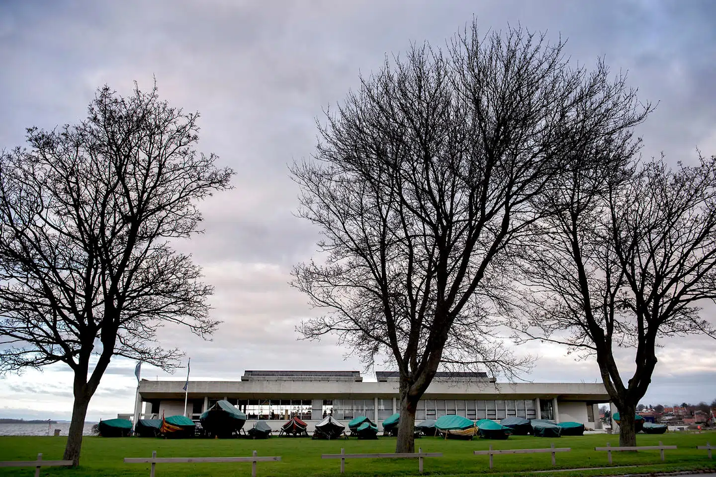 Vikingeskibshallen set fra land. De mange klinkbyggede små og større både, som gennem årene er bygget på museets eget bådeværft, er trukket på land og dækket til for vinteren. Om sommeren bruges de til sejlads på fjorden som en del af museets publikumsaktiviteter.