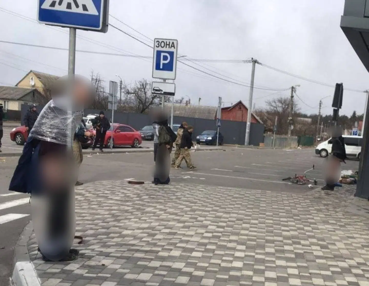 Tre personer er blevet tapet fast til stolper foran et supermarked i Romanivka i Irpin. I baggrunden ses personer i militæruniform. Det er dog ikke bekræftet, at der er tale om soldater fra den ukrainske hær.