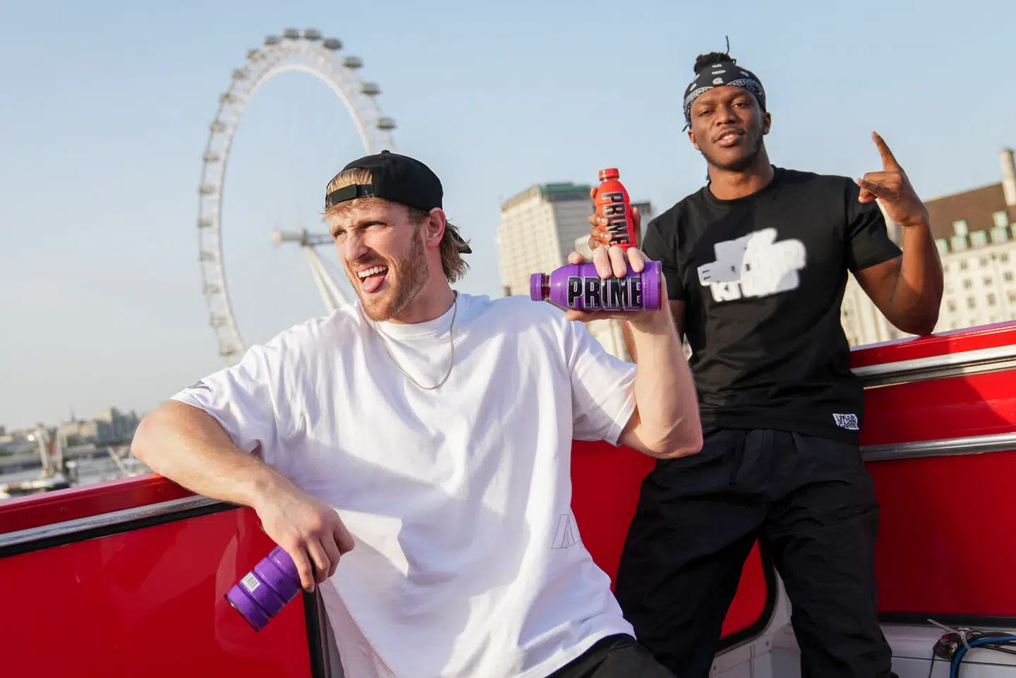 Logan Paul og KSI, poser på dækket af en åben bus, hvorfra de kaster Prime ned til de mange fremmødte.