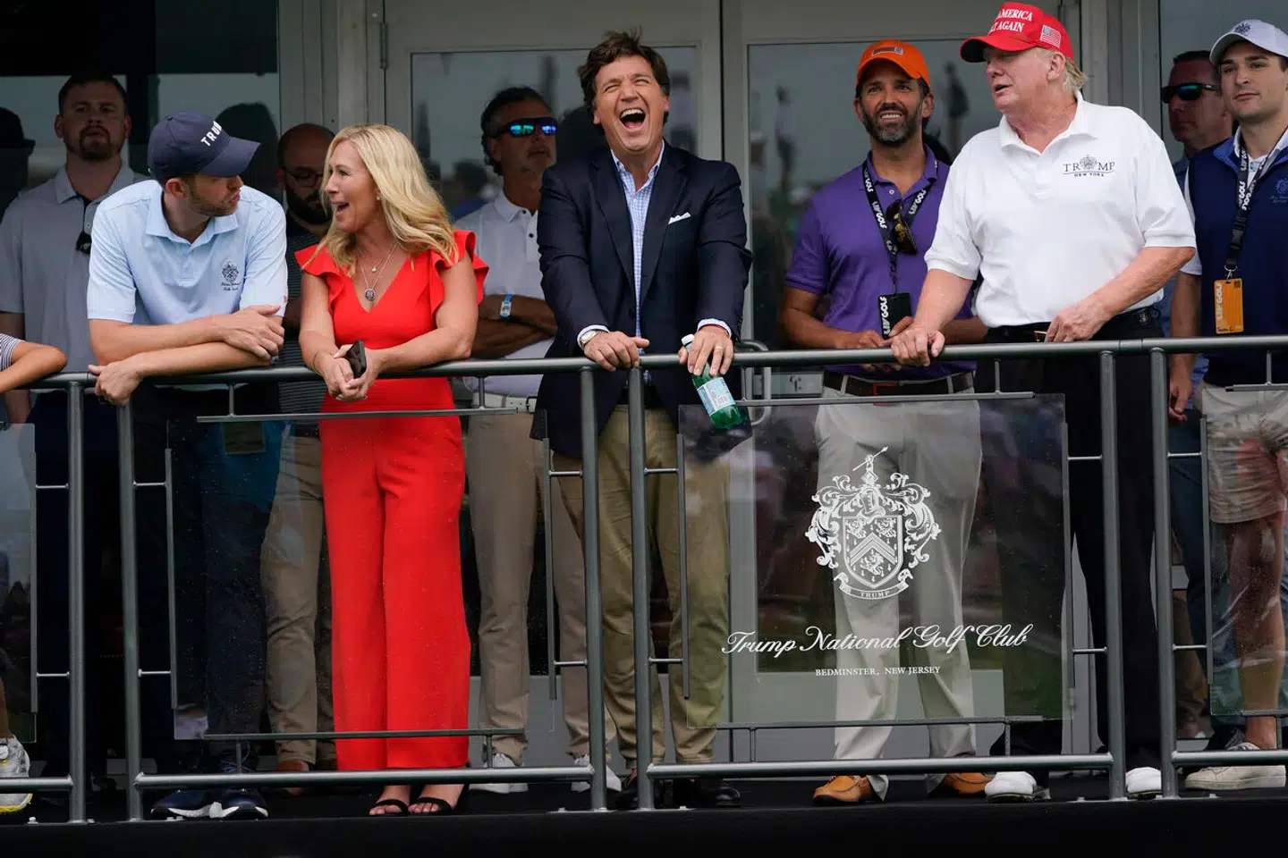 En storgrinende Tucker Carlson omgivet af Donald Trump og sønnerne Eric Trump (i hvdt) og Donald Trump jr. (i lilla) samt den fremtrædende republikanske politiker Marjorie Taylor Greene.