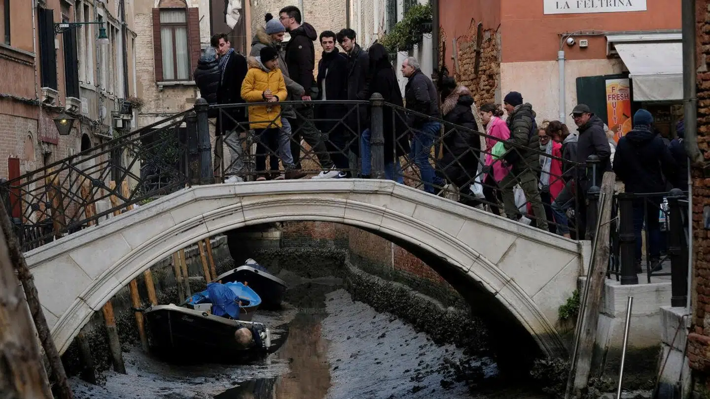 Turister krydser en bro i Venedig, mens de kigger ned på en betydeligt tom kanal, takket være lavvande. Foto: REUTERS/Manuel Silvestri