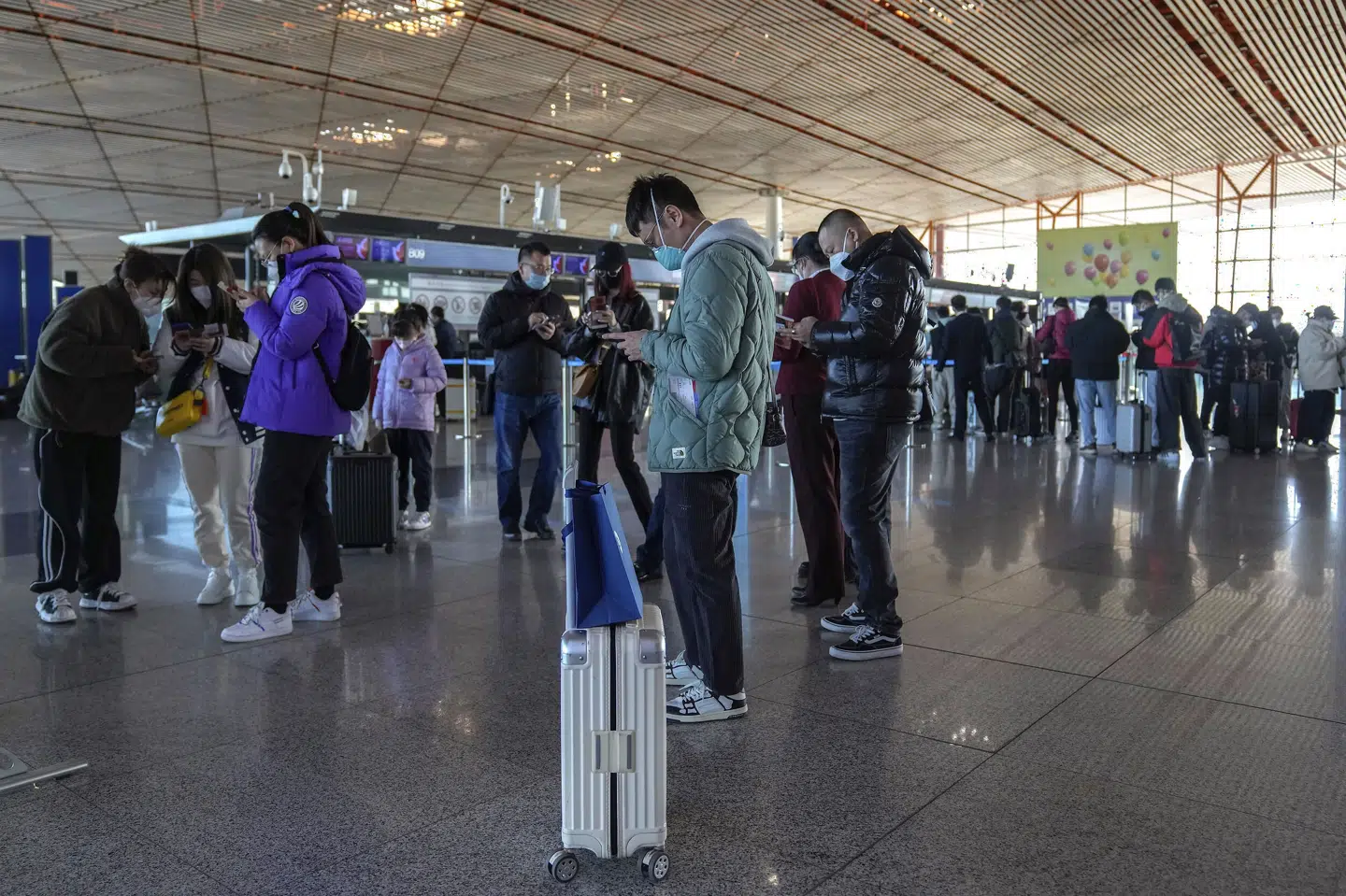 Rejsende med mundbind og smartphones, der viser deres sundhedstilstand, checker ind i Capital International Airport i Beijing. Andy Wong/Ritzau Scanpix