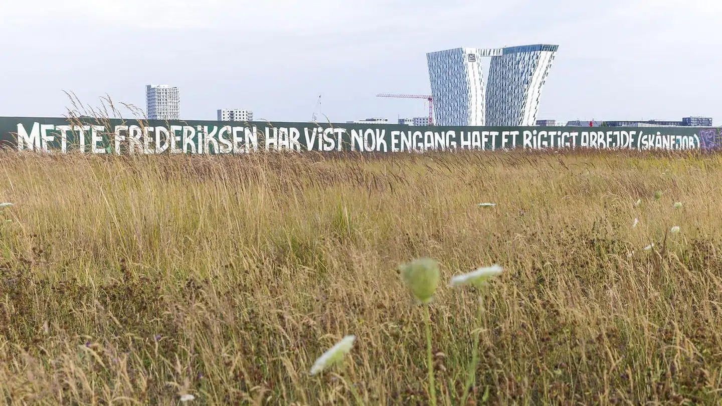 Fælledby byggepladshegn, hvor der står, .Mette Frederiksen har vist nok engang haft et rigtigt arbejde (skånejob), set fra Amager Fælled. (Arkivfoto: Scanpix)