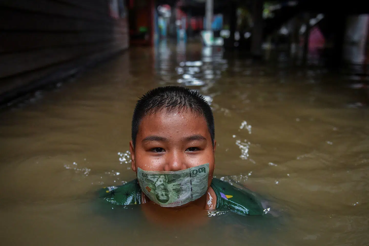 En dreng leger med en 20-bathseddel i munden på en oversvømmet vej i Nonthaburi nær Bangkok i Thailand.