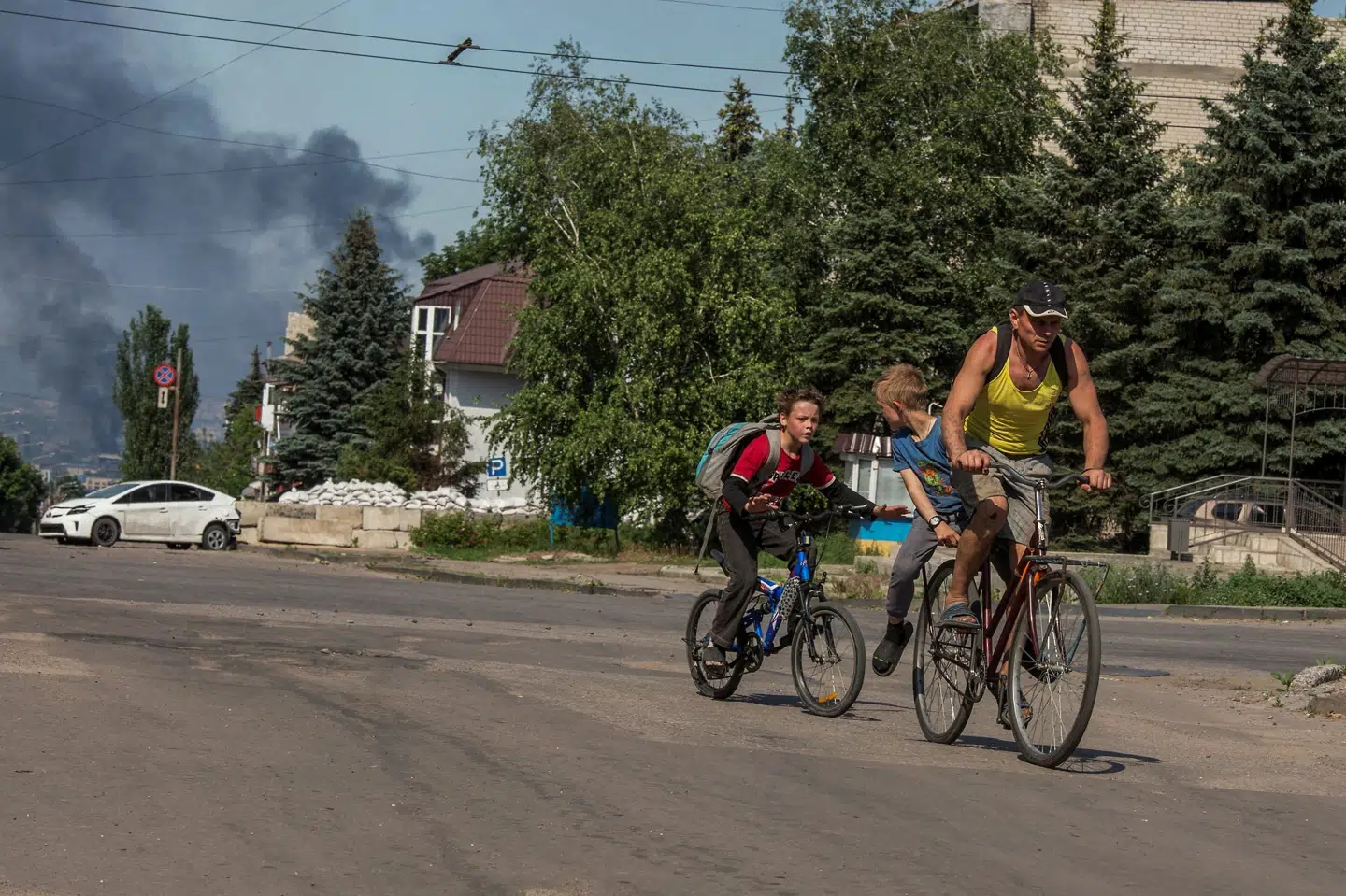 To børn og en mand cykler, mens røg fra et bombardement stiger op i baggrunden i den ukrainske by Lysytjansk i regionen Luhansk i juni i år. Stringer/Reuters