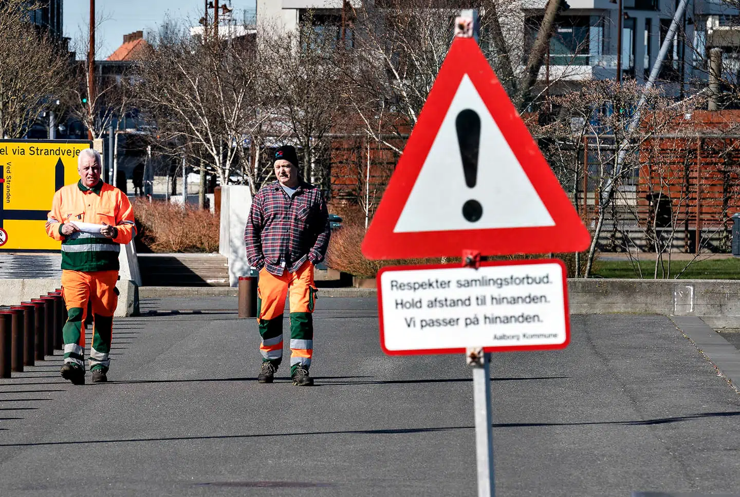 To medarbejdere fra Aalborg Kommune ved advarselsskilt med samlingsforbud ved havnefronten i Aalborg, lørdag den 21. marts 2020. Langs hele havnen i Aalborg var der god afstand mellem de mange folk der var ude og nyde vejret. På grund af COVID-19 er befolkningen blevet bedt om så vidt muligt at holde sig indendørs og udendørs aktiviteter i det flotte forårsvejr skal foregå med god afstand.. (Foto: Henning Bagger/Ritzau Scanpix)