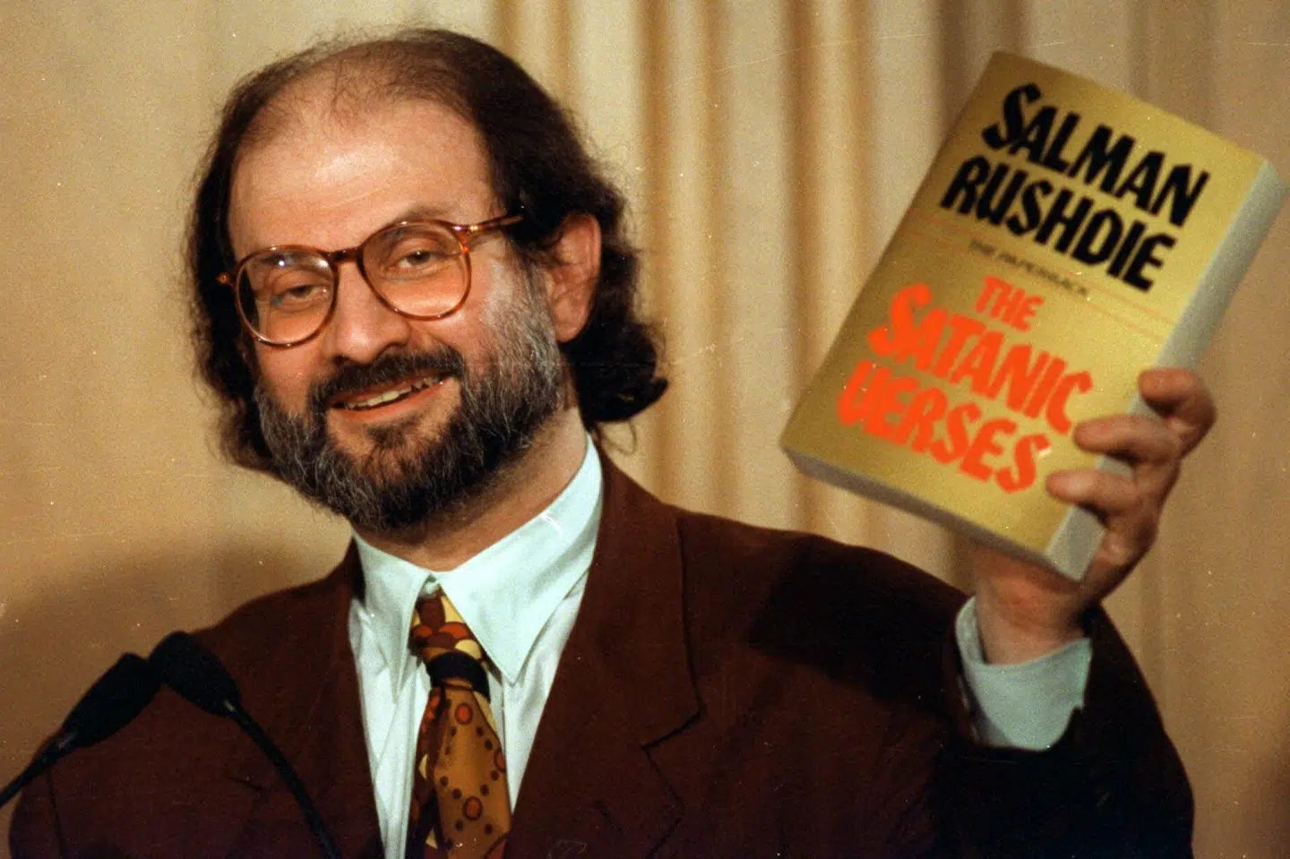 Salman Rushdies bog De sataniske vers udløste kort efter udgivelsen i 1988 demonstrationer verden over. Efter et angreb på Rushdie fredag er den skudt helt op i toppen af Saxos bestsellerliste. Billedet viser den i dag 75-årige forfatter fotograferet med sin kontroversielle bog i 1992. Ron Edmonds/Ritzau Scanpix