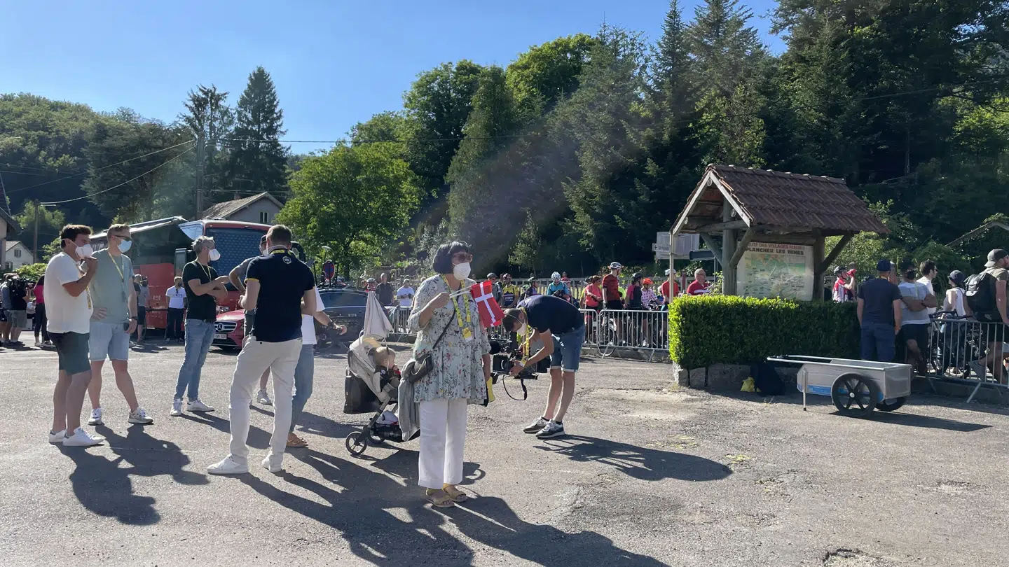 Rosa venter med dannebrog i hånden på svigersønnen Jonas Vingegaard i området, hvor Tourens holdbusser er parkeret.