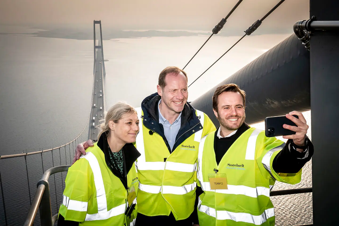 Tour de France-løbsdirektøren Christian Prudhomme (i midten) står her med transportminister Trine Bramsen og erhvervsminister Simon Kollerup. I anledningen af, at der var 100 dage til den danske Tour de France-start, besøgte de en af pylonerne på Storebæltsbroen.