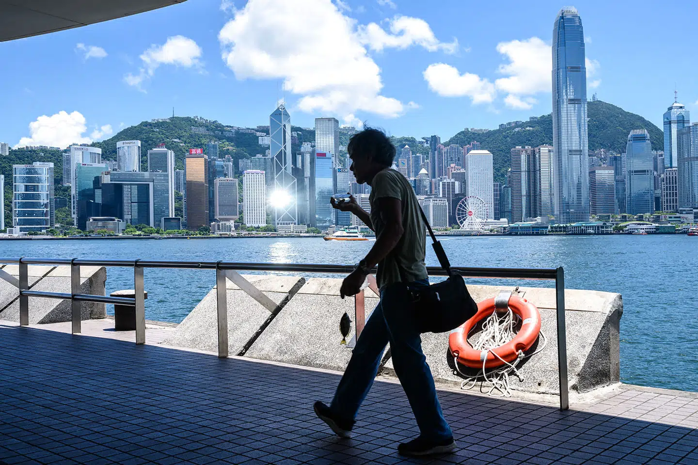 En lystfisker har en fisk på krogen, mens han vandrer langs promenaden ved havnen i Victoria i Hongkong den 13. juli 2020