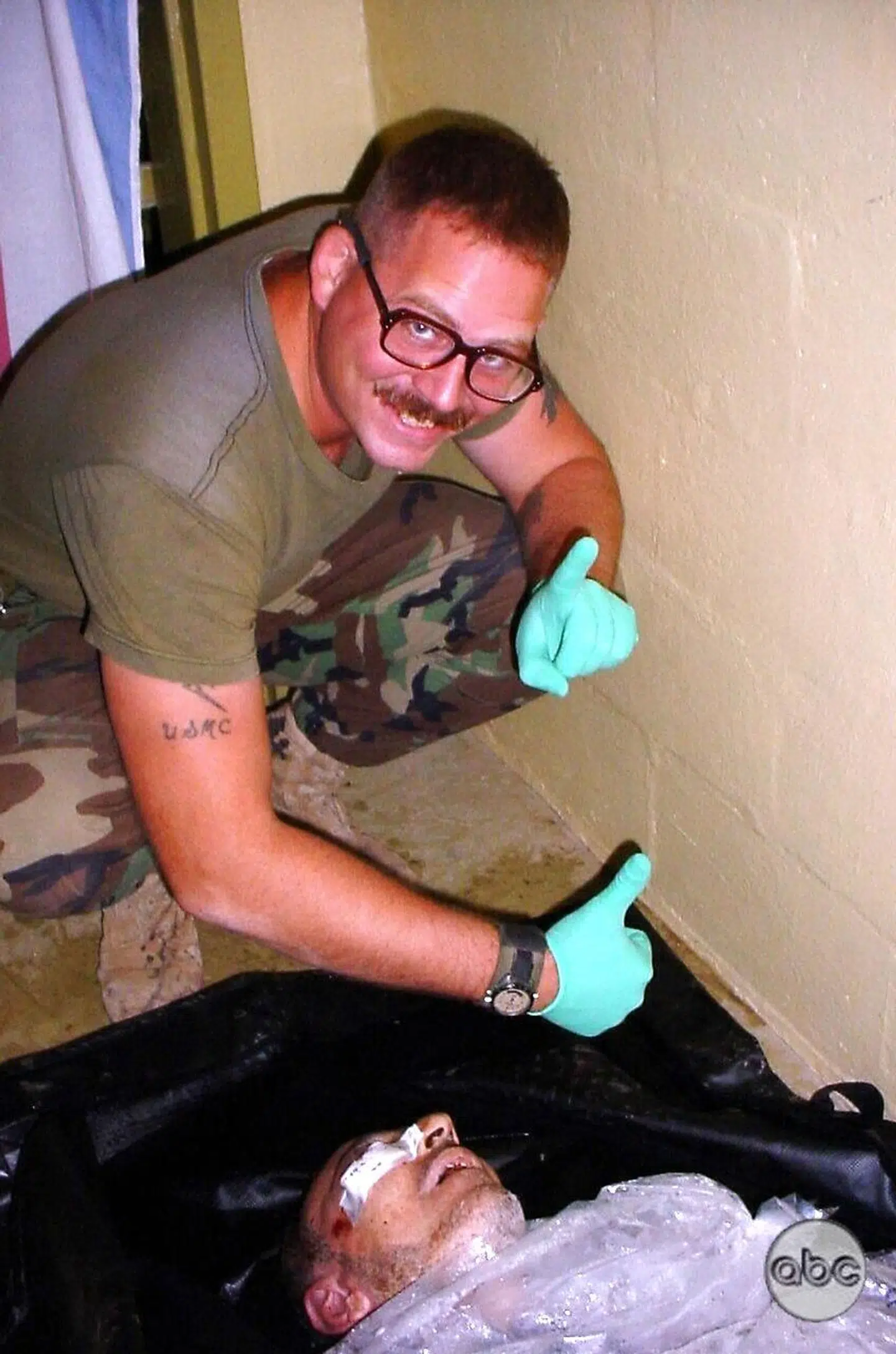 En amerikansk soldat giver 'thumbs up' ved en afdød irakisk fange i Abu Ghraib-fængslet i Irak i 2004.