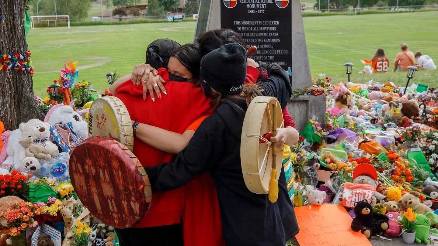 En massegrav med de jordiske rester af 215 børn blev fundet ved en tidligere skole for indfødte i British Columbia. Her krammer nogle indfødte foran et mindested, der er etableret for at ære børnene.