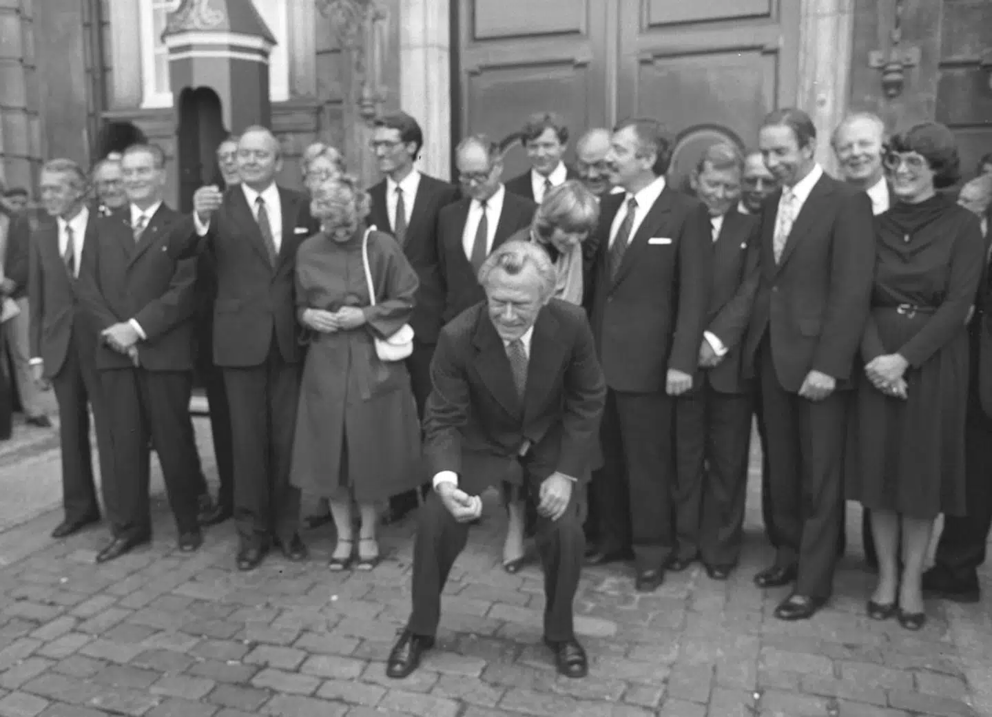 Poul Schlüter præsenterer sin nye regering på Amalienborg Slotsplads. Her samler han de lykkeskillinger op, som de omkringstående har kastet til ham.