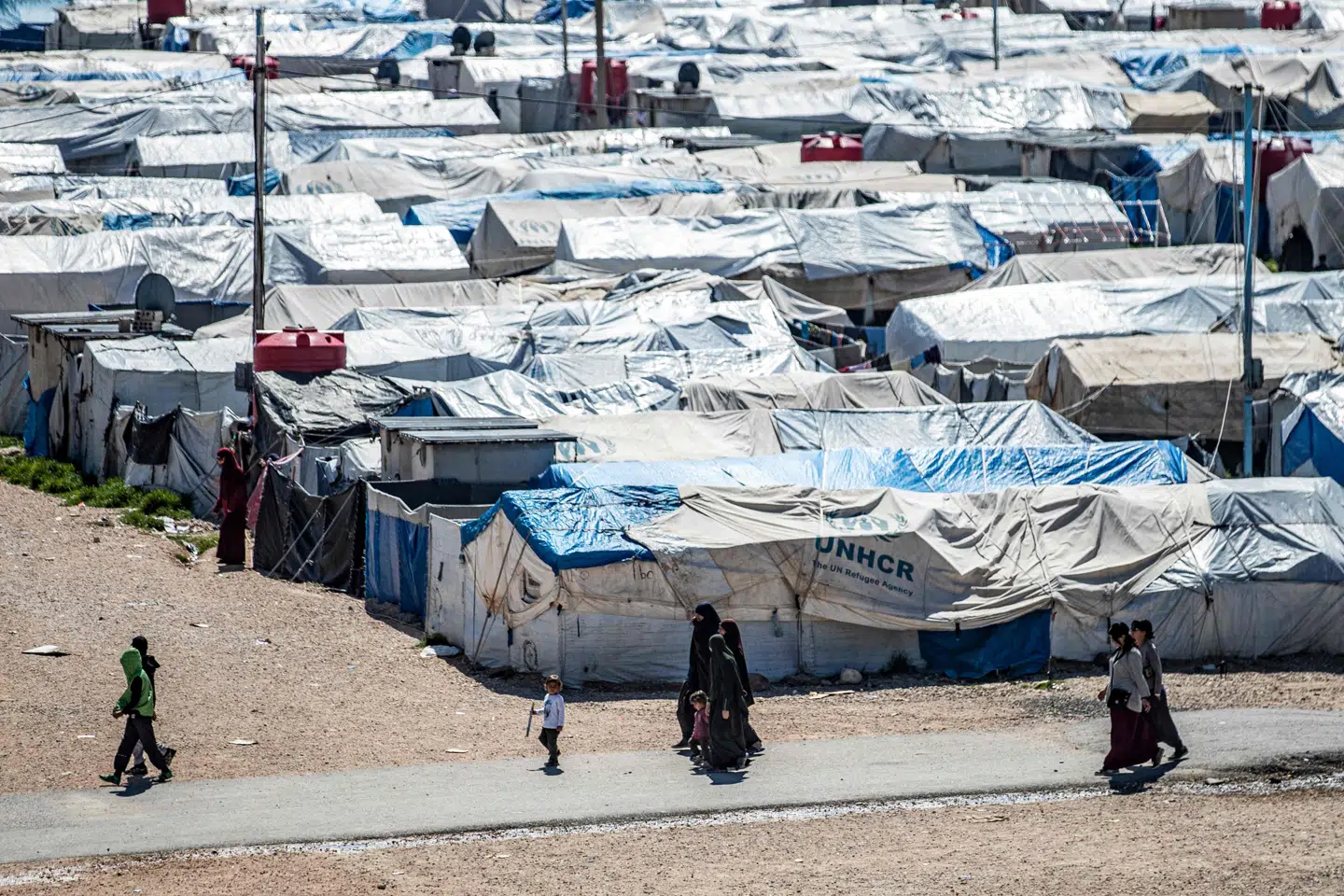 Women and children walk at Camp Roj, where relatives of people suspected of belonging to the Islamic State (IS) group are held, in the countryside near al-Malikiyah (Derik) in Syria's northeastern Hasakah province, on March 28, 2021. - Roj, one of two Kurdish-run displacement camps housing foreign family members of suspected IS fighters, is smaller and better guarded than its overcrowded counterpart Al-Hol, which has been rocked by assassinations and breakout attempts in recent months. (Photo by Delil SOULEIMAN / AFP)