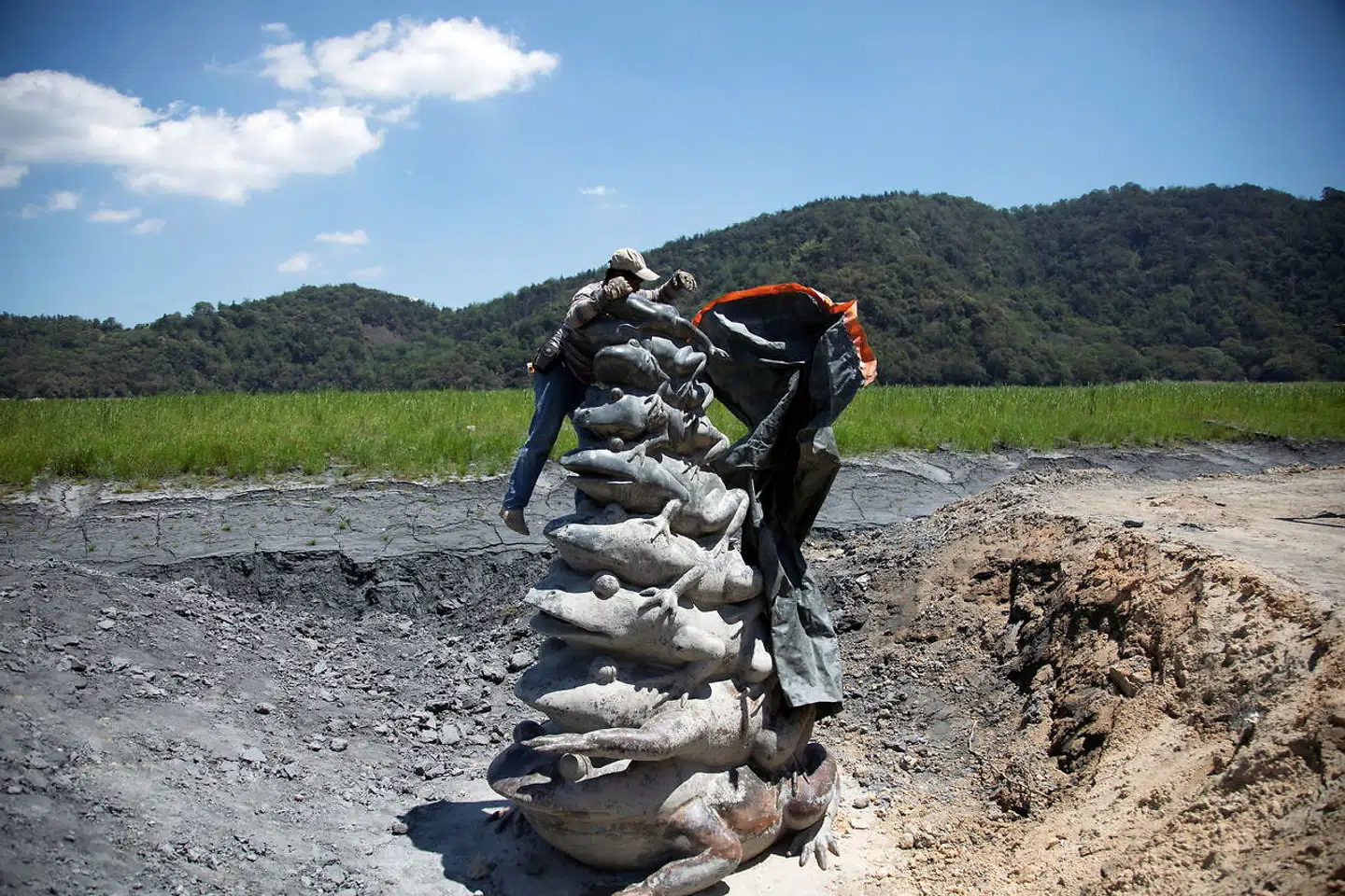 En mand fjerner coveret fra statuen 'Nine Frog Stack', som normalt ligger under vand.