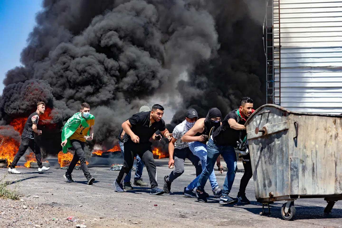 Unge palæstinensere bygger barrikader med affaldscontainere under sammenstød med israelske soldater syd for byen Nablus på Vestbredden fredag. Ti er dræbt og langt flere såret, oplyser palæstinensiske sundhedsmyndigheder. Jaafar Ashtiyeh/Ritzau Scanpix