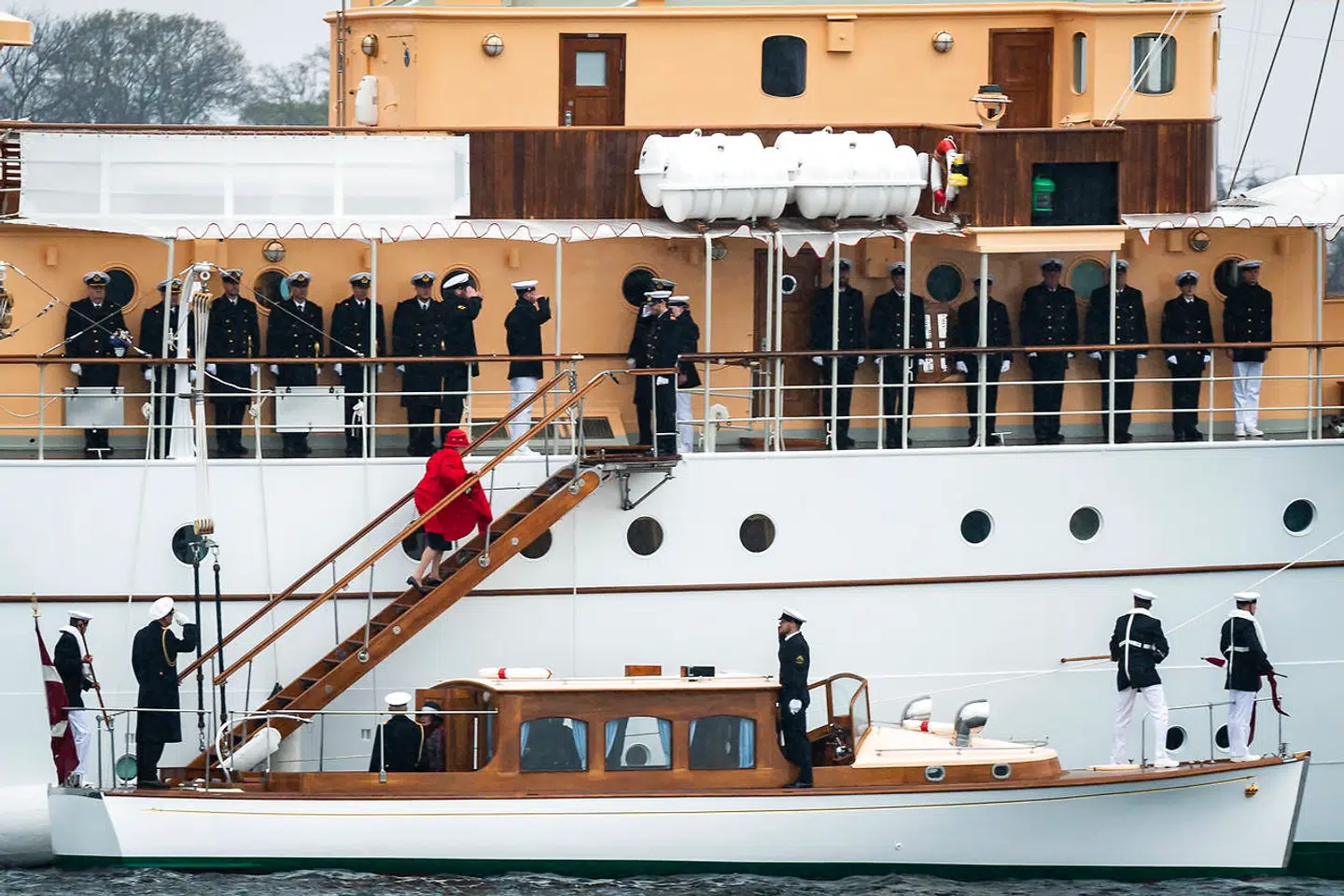 Her går en dronning Margrethe klædt i rødt officielt ombord på Kongeskibet Dannebrog i Københavns Havn.