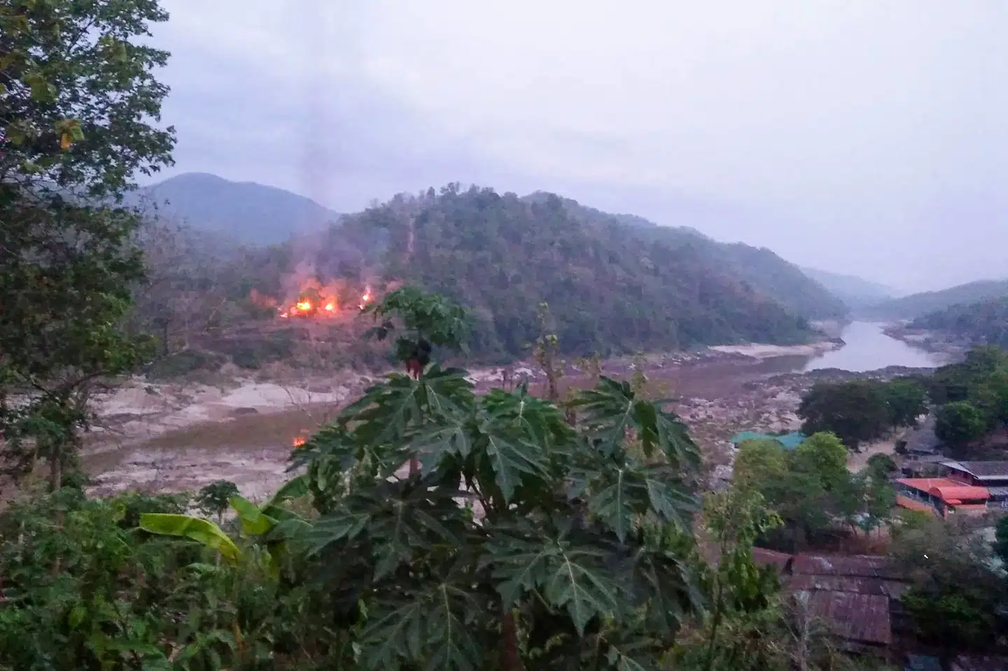 Et billede taget fra den thailandske side af grænsen viser en militærbase brænde tæt på floden Salween, der udgør grænsen mellem Myanmar og Thailand. Militærbasen er blevet angrebet og indtaget af oprørsgruppen Karen National Union (KNU). Handout/Ritzau Scanpix