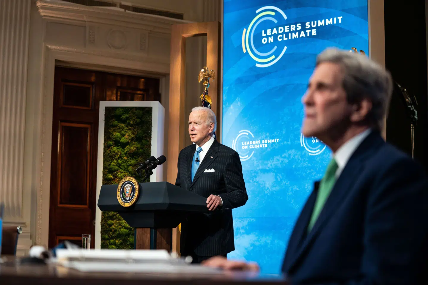 Præsident Joe Biden taler til de øvrige deltagere på et to dage langt klimatopmøde. Mødet blev som følge af coronapandemien holdt virtuelt. I forgrunden den amerikanske præsidents særlige klimaudsending, John Kerry. Pool/Ritzau Scanpix