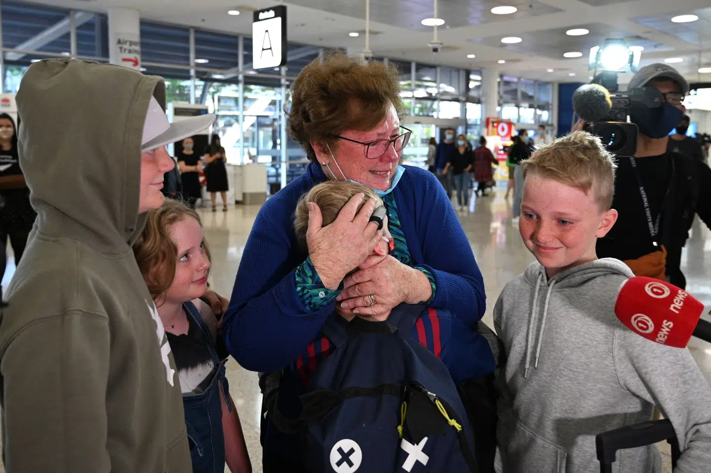 En kvinde omfavner sine familiemedlemmer fra New Zealand i Sydneys internationale lufthavn. Saeed Khan/Ritzau Scanpix