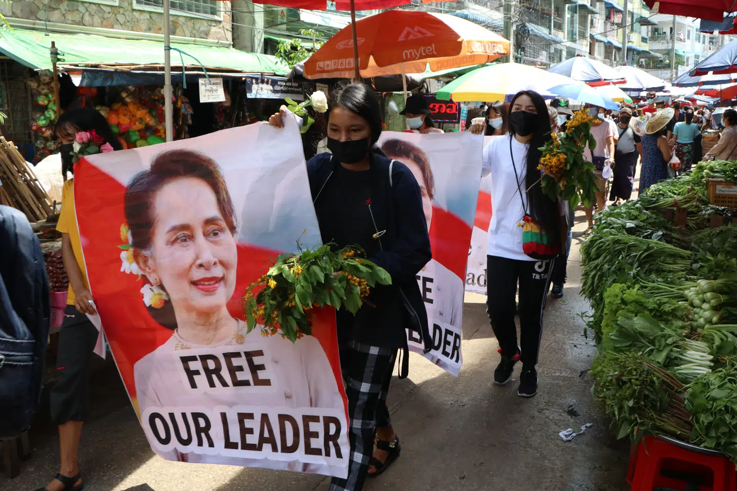 Demonstranter går gennem et marked i bydelen Kamayut i Myanmars storby Yangon. Befri vores leder, står der på plakaten under et billede af Aung San Suu Kyi. Uncredited/Ritzau Scanpix