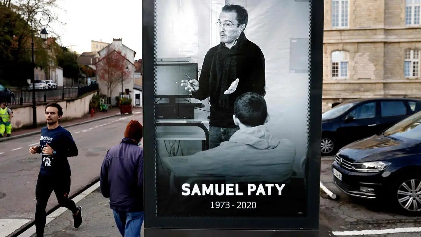 Gående går forbi en plakat med skolelæreren Samuel Paty, der blev myrdet den 16. oktober 2020, for at have vist et billede af profeten Muhammed til sine elever.