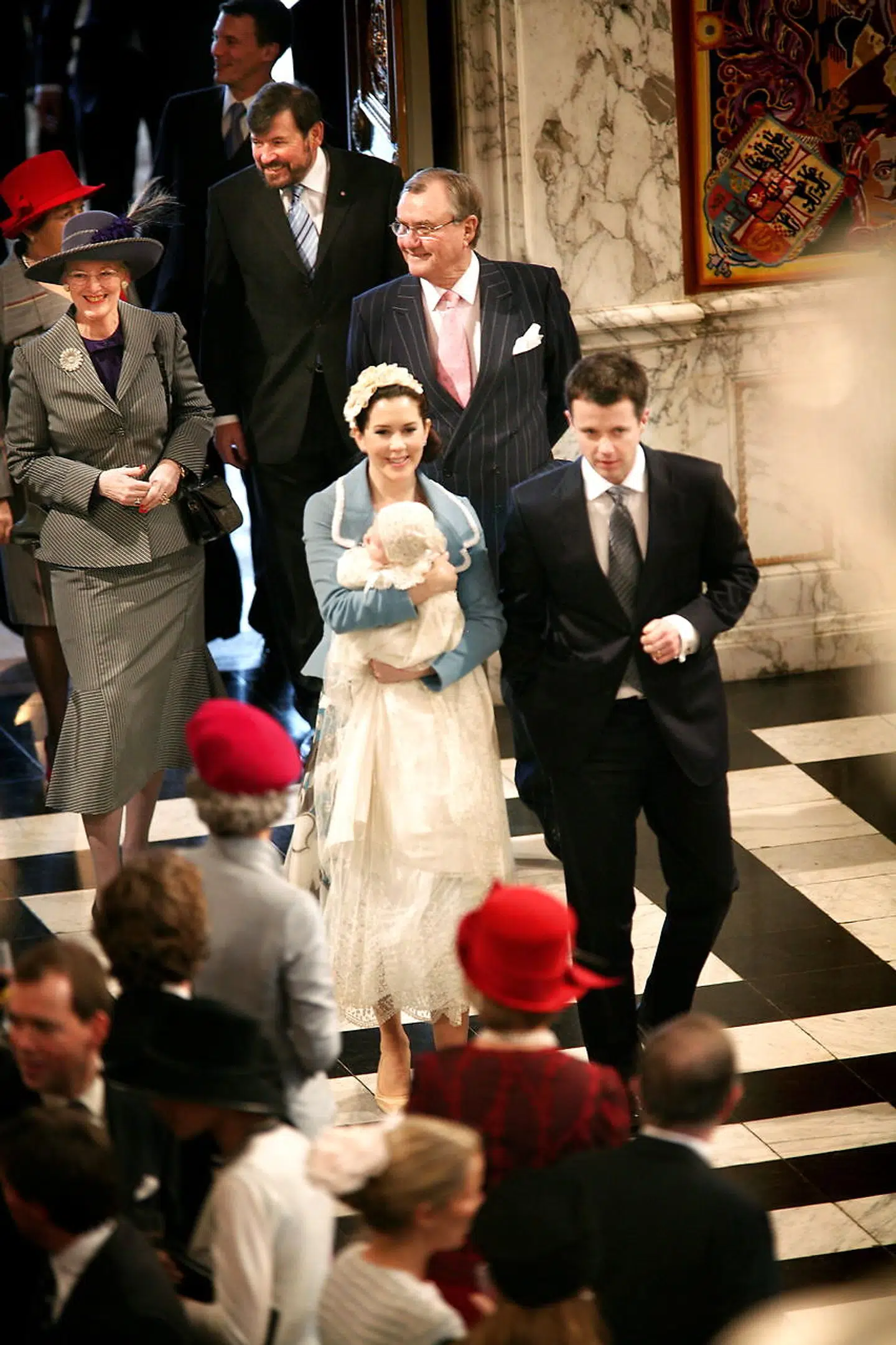 Kronprins Frederik, Kronprinsesse Mary og den lille nydøbte prins Christian Valdemar Henri John ankommer til receptionen i Riddersalen på Christiansborg efter den kongelige barnedåb. Efter kkronprinsparret kommer dronning Margrethe, Prins Henrik, John Donaldson og Susan Donaldson.