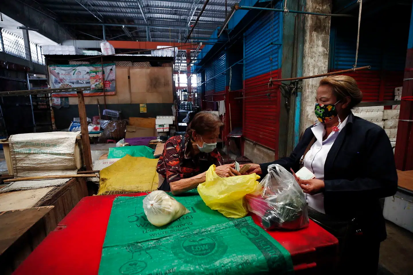 En kvinde køber mad fra en ældre mand, mens handlen stoppes på et af den seks markeder, der ligger tæt på hinanden i Bangkok. De er lukket i tre dage, efter at over 100 er blevet smittet med coronavirus.