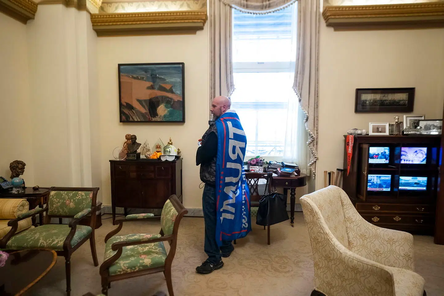 En mand svøbt i et Trump-flag på Nancy Pelosis kontor.