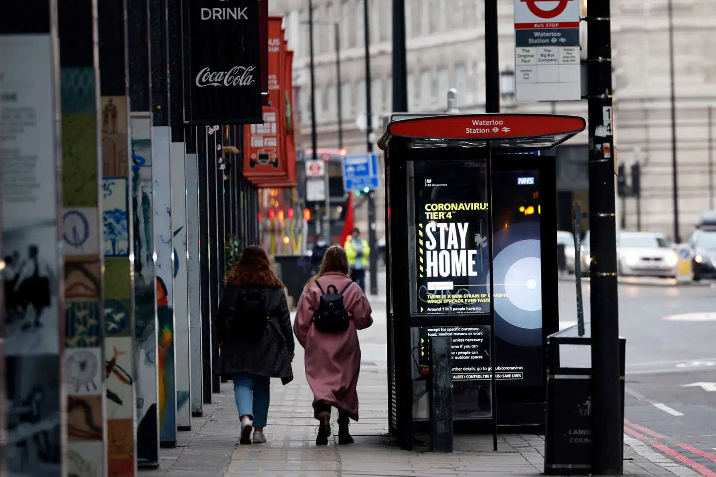 Et par fodgængere passerer tirsdag forbi et busstoppested i det centrale London, hvor en af regeringens kampagne-plakater opfordrer folk til at blive hjemme i løbet af jul og nytår. Tolga Akmen/Ritzau Scanpix