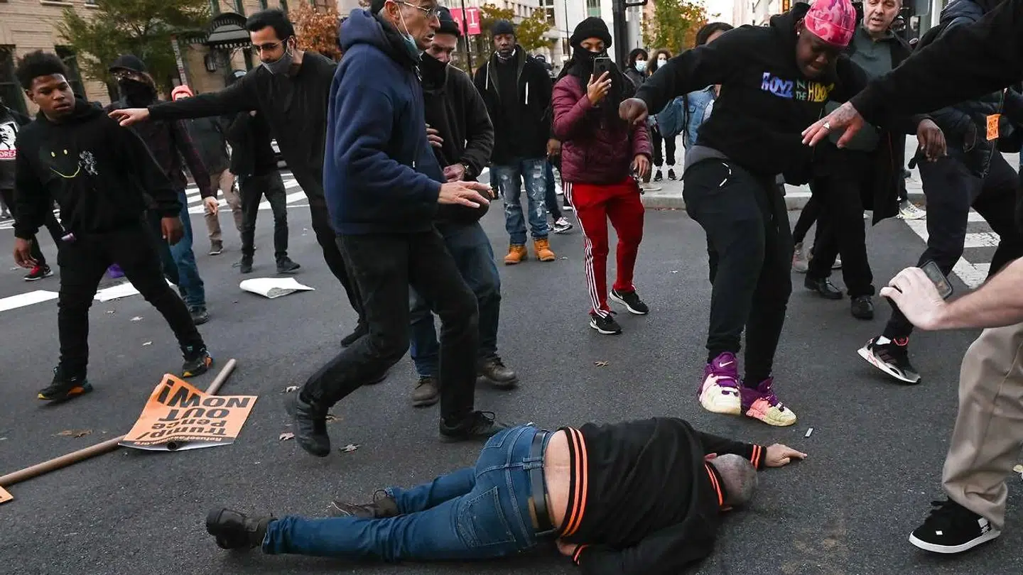 En mørk demonstrant i gang med at trampe en Trump-støtte i hovedet, efter han er blevet slået ud.