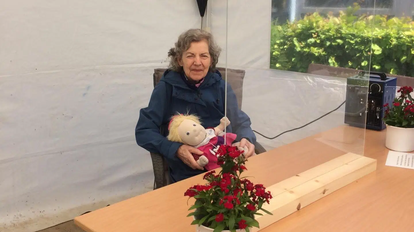 Pia Røges mor ses her i det telt, hvor Pia i foråret kunne besøge sin mor. Hun sidder bag et plexiglas og med sin demensdukke i hånden, der giver tryghed. Foto: Privat.