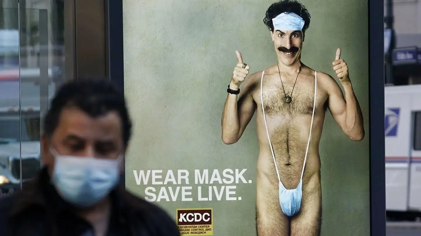A person wearing a mask walks past a bus stop ad on 5th Avenue, October 15, 2020, for the upcoming movie "Borat 2, " featuring actor Sacha Baron Cohen, ahead of its release on October 23. - The poster gives reference to the Covid-19 pandemic by replacing Borat's iconic green 'mankini' with a face mask. (Photo by TIMOTHY A. CLARY / AFP)