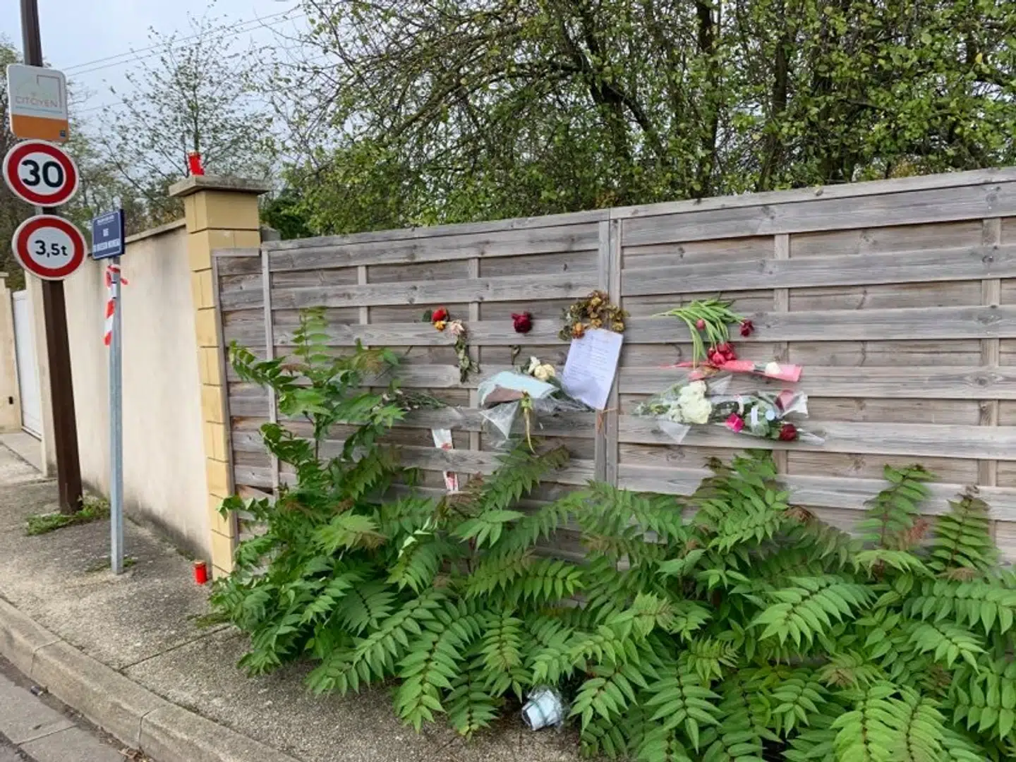 Samuel Paty blev myrdet på Rue du Buisson Moineau tæt på skolen i Conflans-Sainte-Honorine, som han underviste på. For enden af vejen er der hængt sedler og blomster op til minde om den afdøde lærer.
