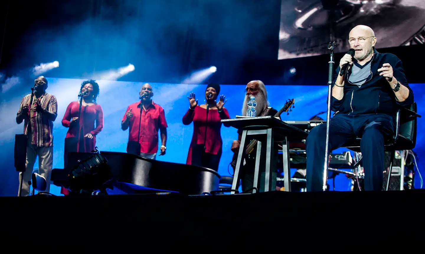 På grund af sit dårlige helbred sidder Phil Collins ned, når han optræder.