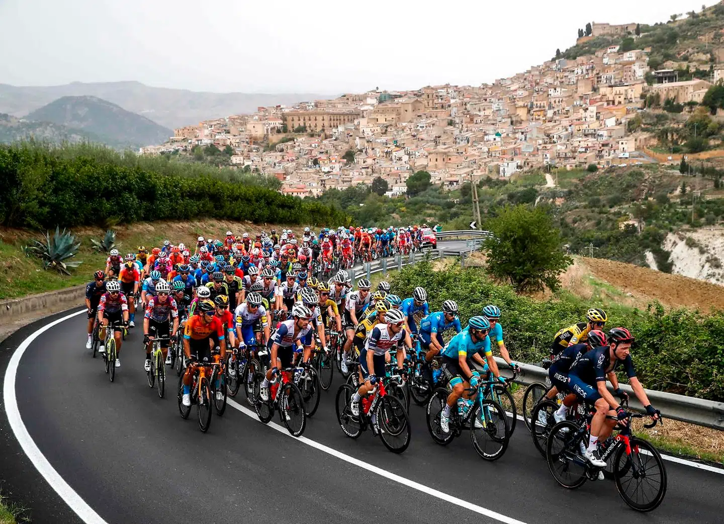TOPSHOT - (From R) Team Ineos rider Great Britain's Tao Geoghegan Hart, Team Ineos rider Ecuador's Jhonatan Narvaez, Team Jumbo rider Netherlands' Antwan Tolhoek and the pack ride past the village of Leonforte (Rear) on October 5, 2020 during the 3rd stage of the Giro d'Italia 2020 cycling race, a 150-kilometer route between Enna and volcano Etna, Linguaglossa-Piano Provenzana, Sicily. (Photo by Luca Bettini / AFP)