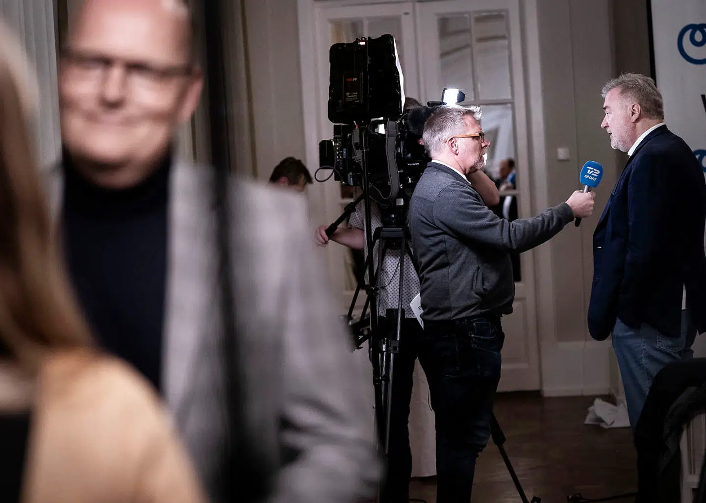 Bjarne Riis bliver interviewet forrest, mens Lars Seier Christensen bliver det i baggrunden ved pressemødet på Hotel D'Angleterre i januar. Her blev det meldt ud, at Virtu Cycling blev en del af NTT Pro Cycling.