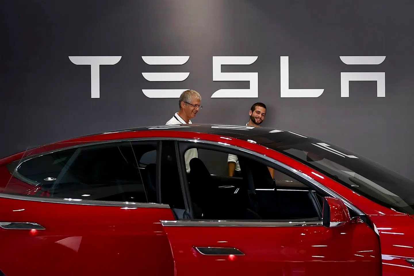 Two man stand in front of a Tesla logo behind the Tesla Model S at the electric carmaker Tesla showroom of El Corte Ingles store in Lisbon, on September 1, 2017. / AFP PHOTO / PATRICIA DE MELO MOREIRA