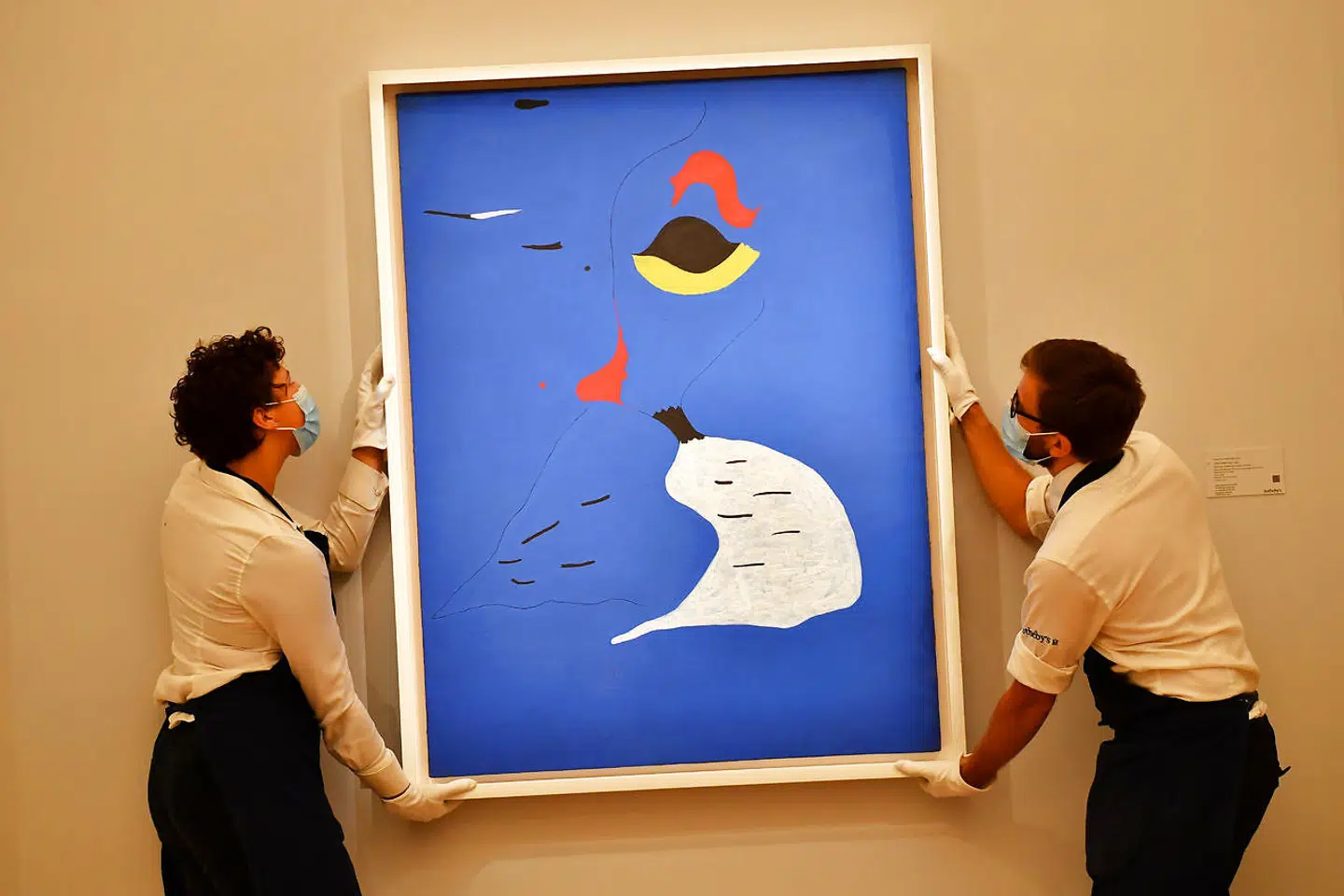 To assistenter er ved at hænge Joan Mirós maleri 'Maleri (Kvinde i rød hat)' op i London.
