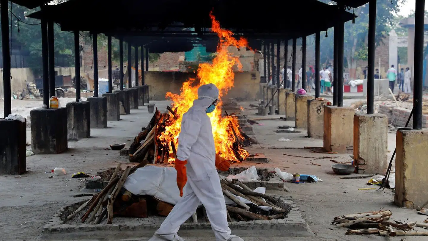 En medarbejder går foran et bål med lig i New Delhi i Indien