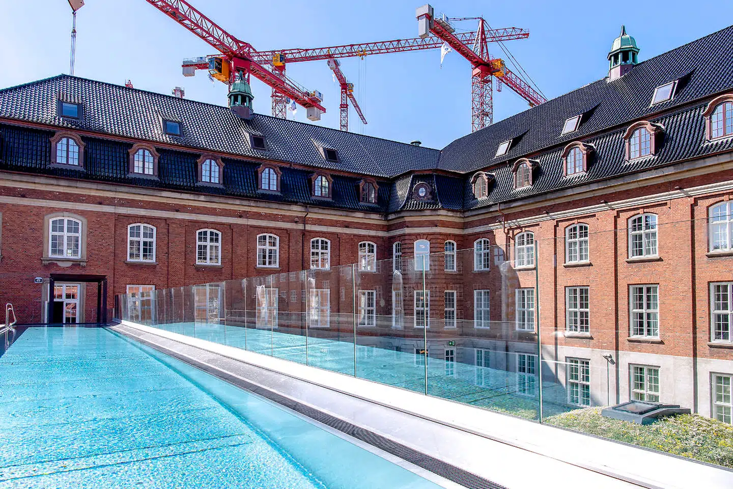 Udsigt mod den nyanlagte, sortglasserede tegltag på Villa Copenhagen. Kvistene og elevatortårnene er falset og inddækket med kobber. I forgrunden ses en 25 meter lange, udendørs pool, som bliver opvarmet med genbrugsvarme fra hotellet.