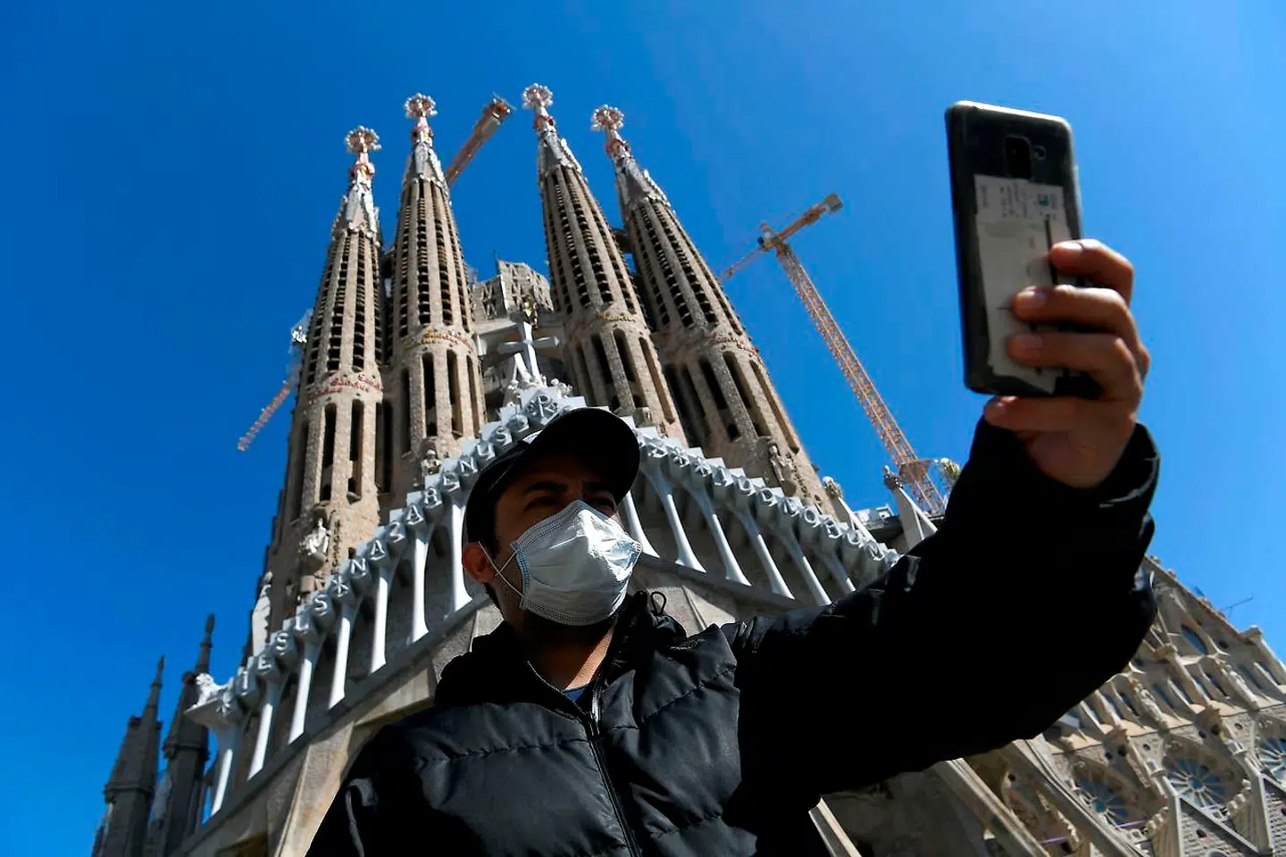 En turist tager en corona-selfie foran den berømte kirke La Sagrada Familia i Barcelona.(Photo by LLUIS GENE / AFP)