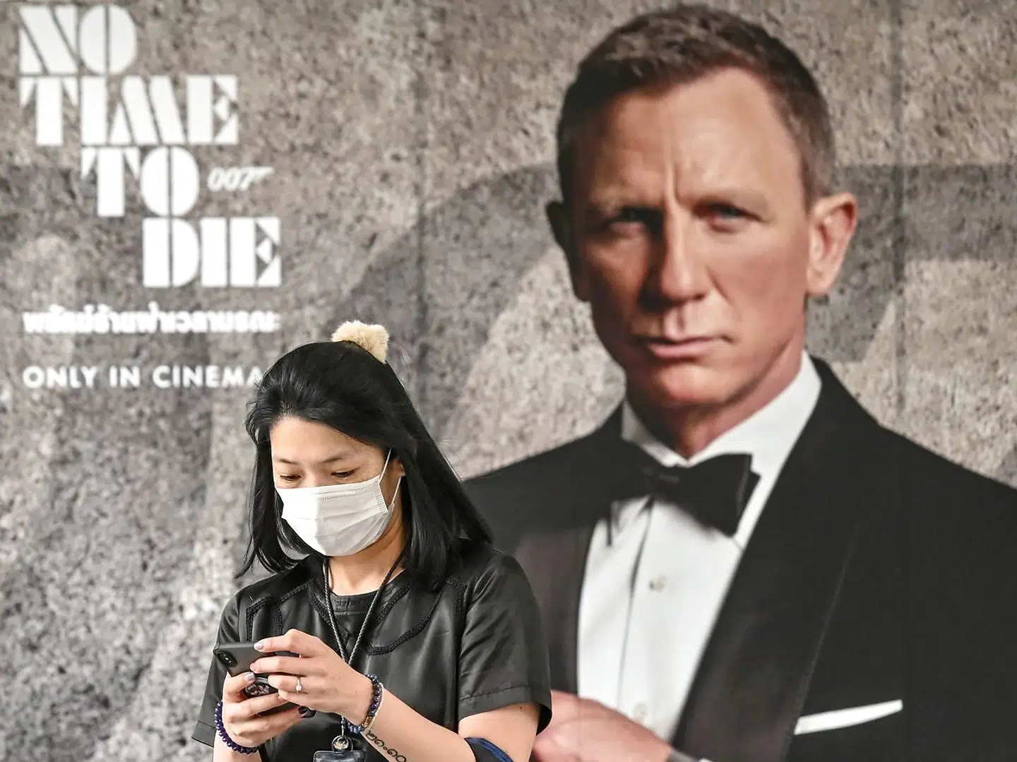 En kvinde iført an ansigtmaske, går forbi en plakat for den nye Jams Bondfilm 'No Time to Die' i Bangkok.