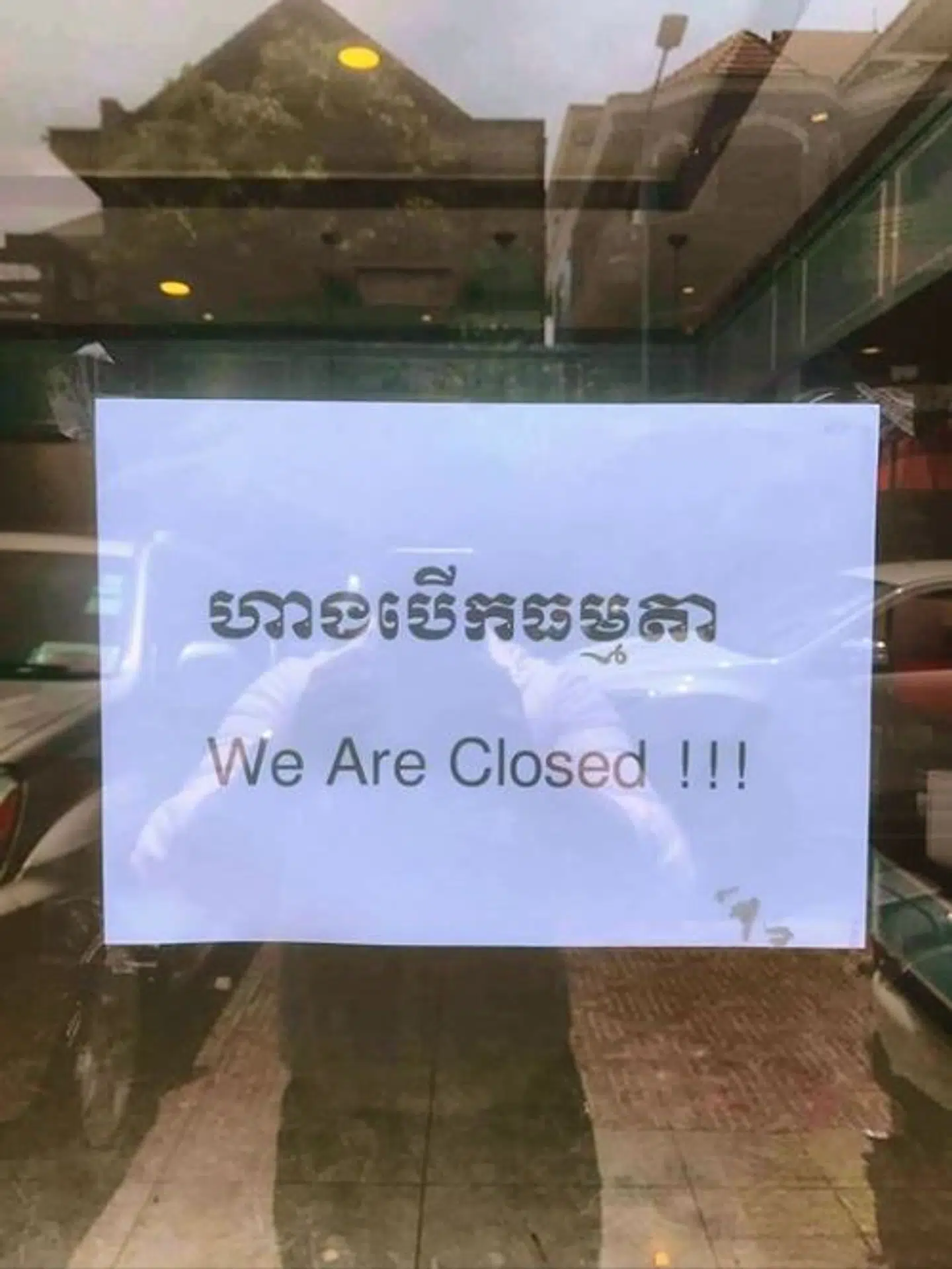 Skiltet, der hænger på butiksruder og døre i Cambodia, hvor der på engelsk står, at der er lukket, og på cambodiansk står, at der er åbent som normalt.