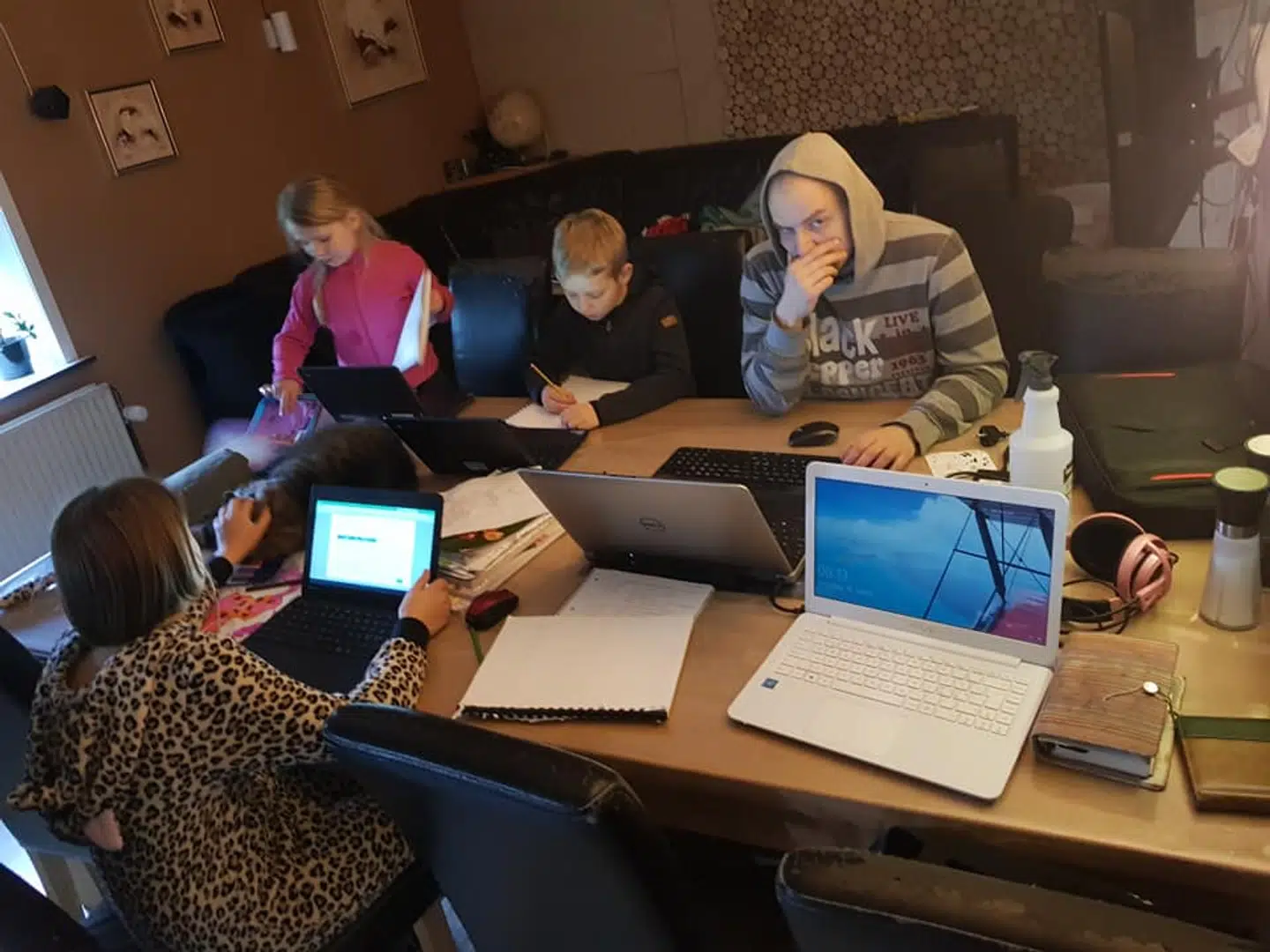 De tre skolebørn og deres far samlet om spisebordet, mens børnene laver skoleopgaver og far prøver at koncentrere sig om arbejde