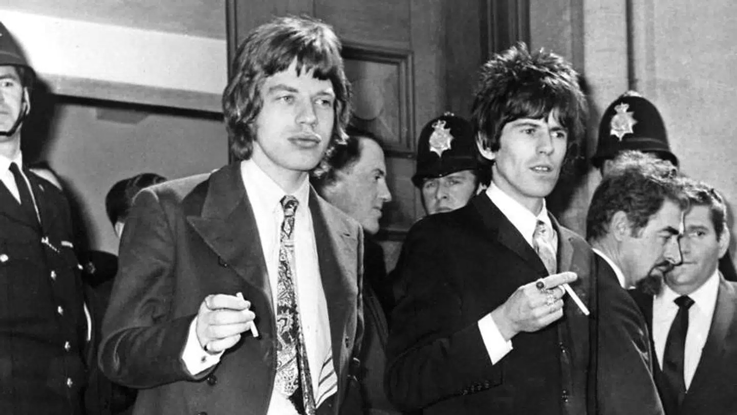 Mick Jagger og Keith Richards for sig en smøg foran retsbygningen i Chichester 11. maj 1967. Der var i retten på grund af en tiltale for ulovlig besiddelse af narkotika.
