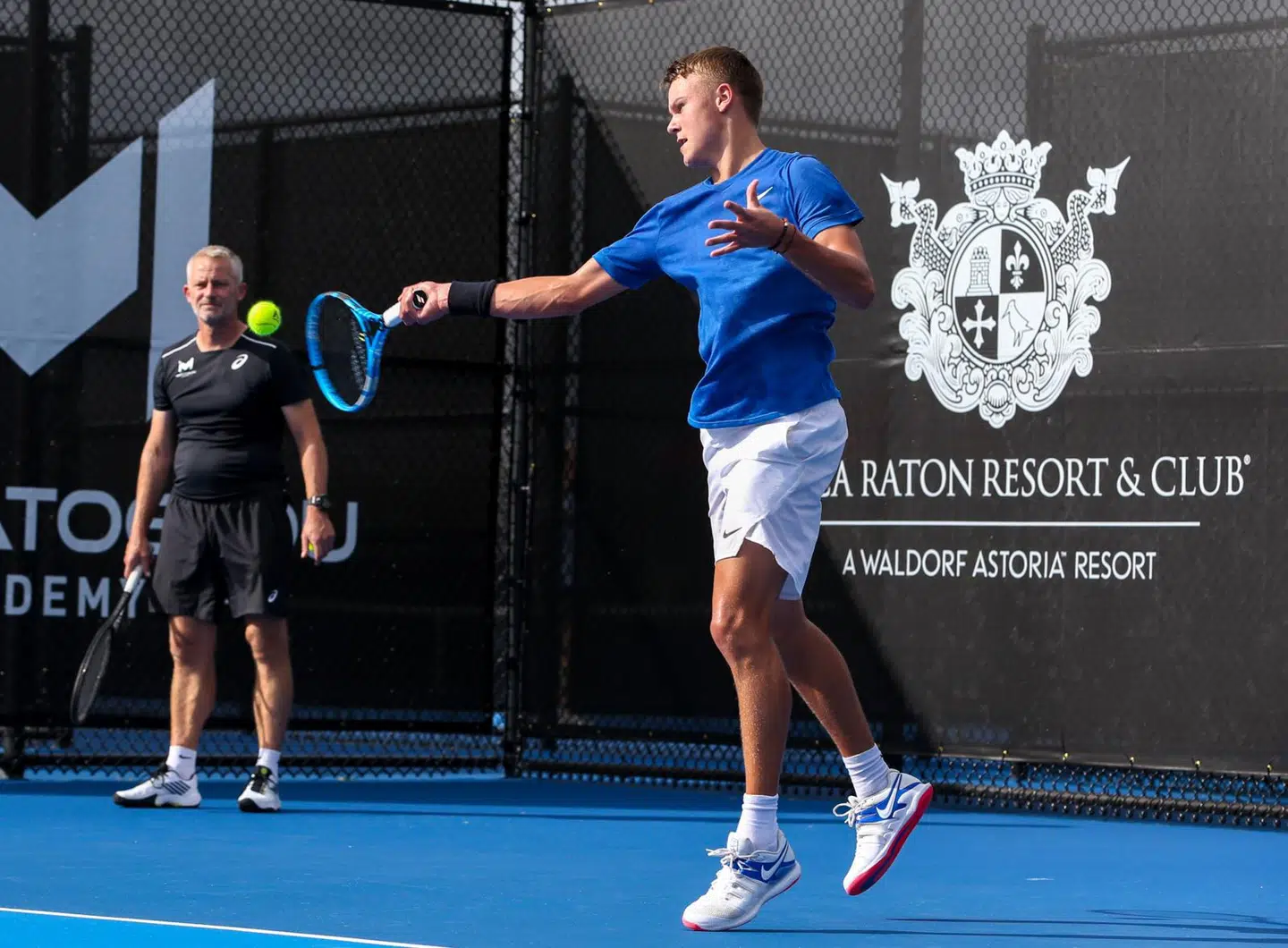Holger Rune i aktion på træningsbanen på Boca Raton Resort & Club i Florida. I hjørnet - klædt i sort - ses træner Lars Christensen.
