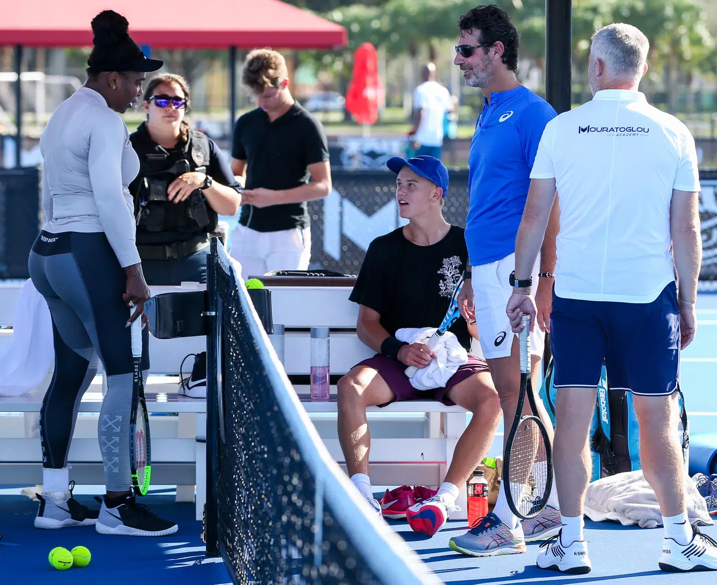 Der bliver passet godt på deltagerne i træningslejren på Boca Raton Resort & Club. Bag Serena Williams, til venstre, ses en bevæbnet vagt. Holger Rune sidder på bænken iklædt en blå kasket og ved siden af ham ses tennistræneren Patrick Mouratoglou.