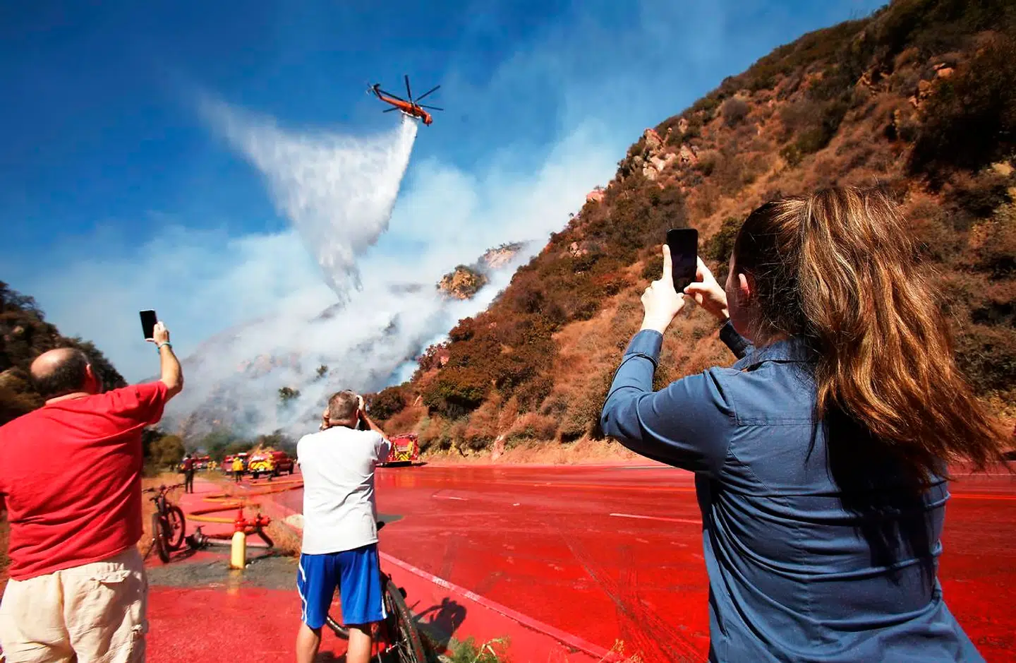 De forsamlede tilskuere har travlt med at fotografere helikopteren, som spreder brandhæmmende materiale på flammerne.